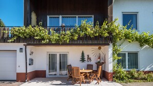 A two-story building with a balcony, a dining area with chairs and a table, and a garage. - Apartment 'Haus Isele' with Mountain View, Terrace and Wi-Fi (Dachsberg)