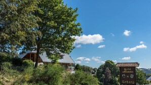 A signboard with text welcoming visitors to Urberg, a house with a sloped roof, surrounded by greenery. - Apartment 'Haus Isele' with Mountain View, Terrace and Wi-Fi (Dachsberg)