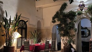 Un comedor con una mesa preparada para dos personas, rodeado de plantas en macetas y un centro de mesa decorativo con velas.