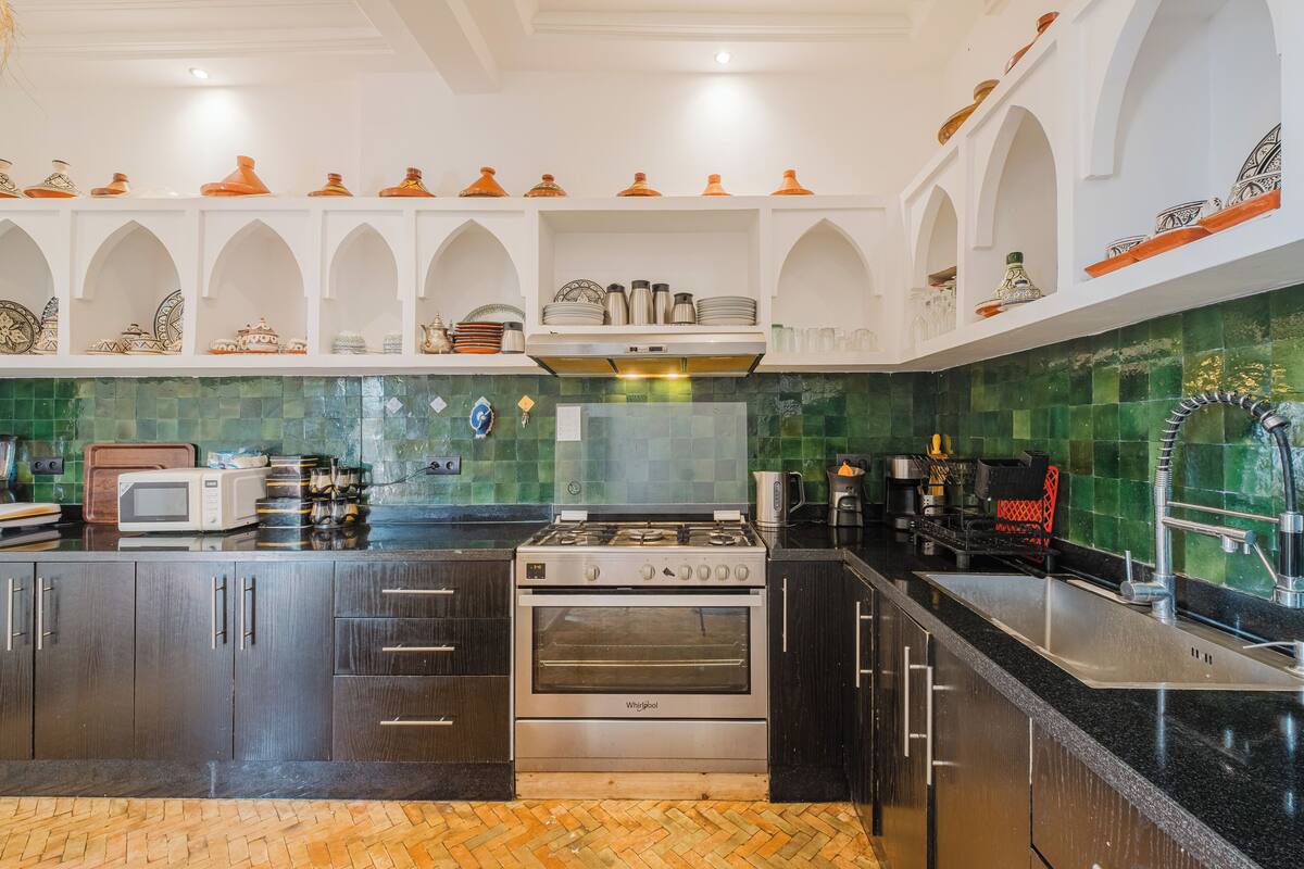 Une cuisine avec des meubles de couleur sombre, une cuisinière Whirlpool, un four à micro-ondes et un dosseret de carrelage vert.