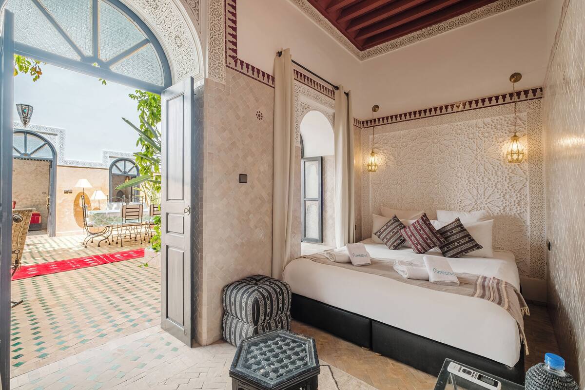 Une chambre spacieuse avec un grand lit, un petit coin salon et une vue sur la cour.
