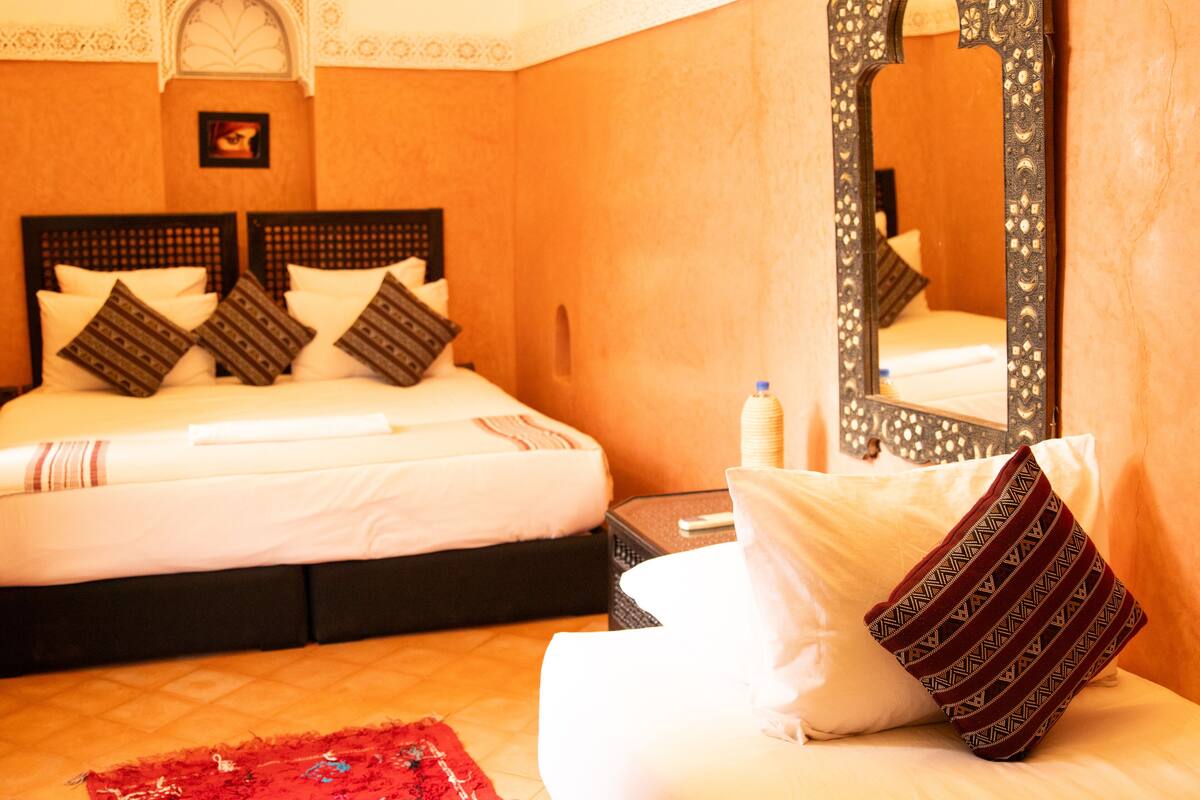 Une chambre d’hôtel avec un lit, des oreillers, une table de chevet, un miroir et un tapis rouge.