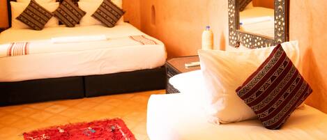 A hotel room with a bed, pillows, a nightstand, a mirror, and a red rug.