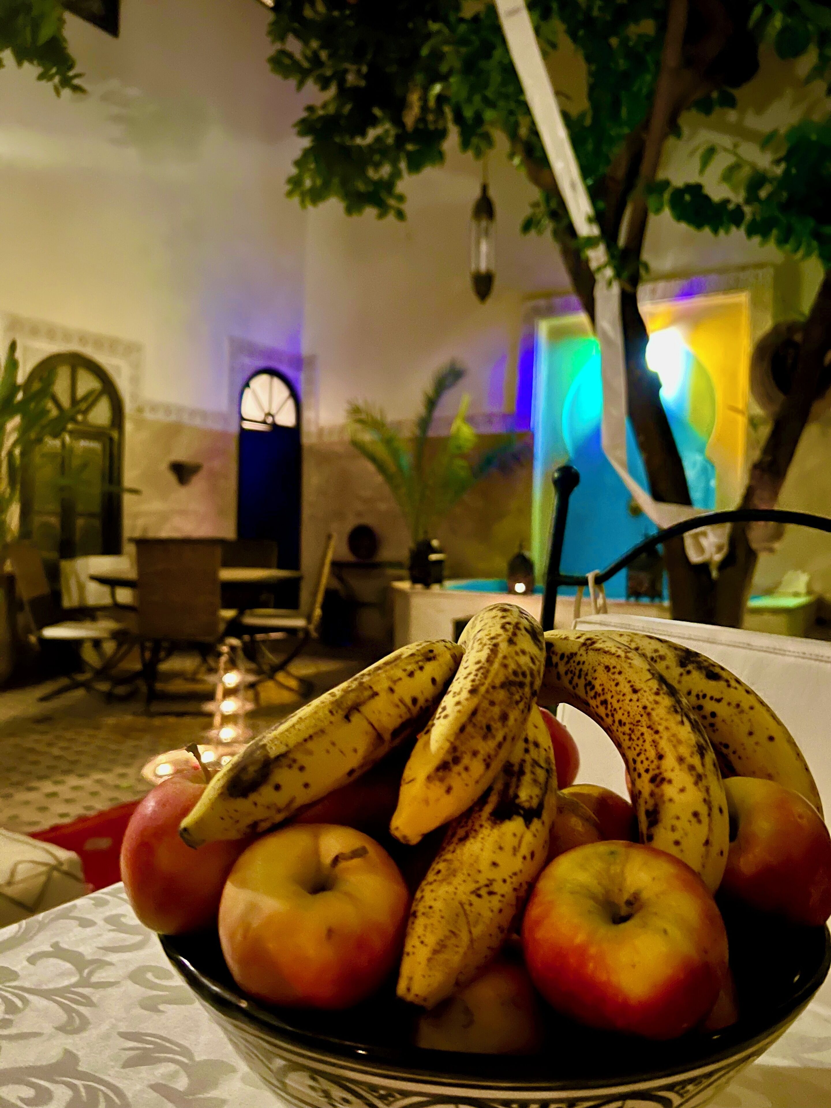 Een schaal fruit op een tafel in een kamer met een eethoek en een sierlijke boom.