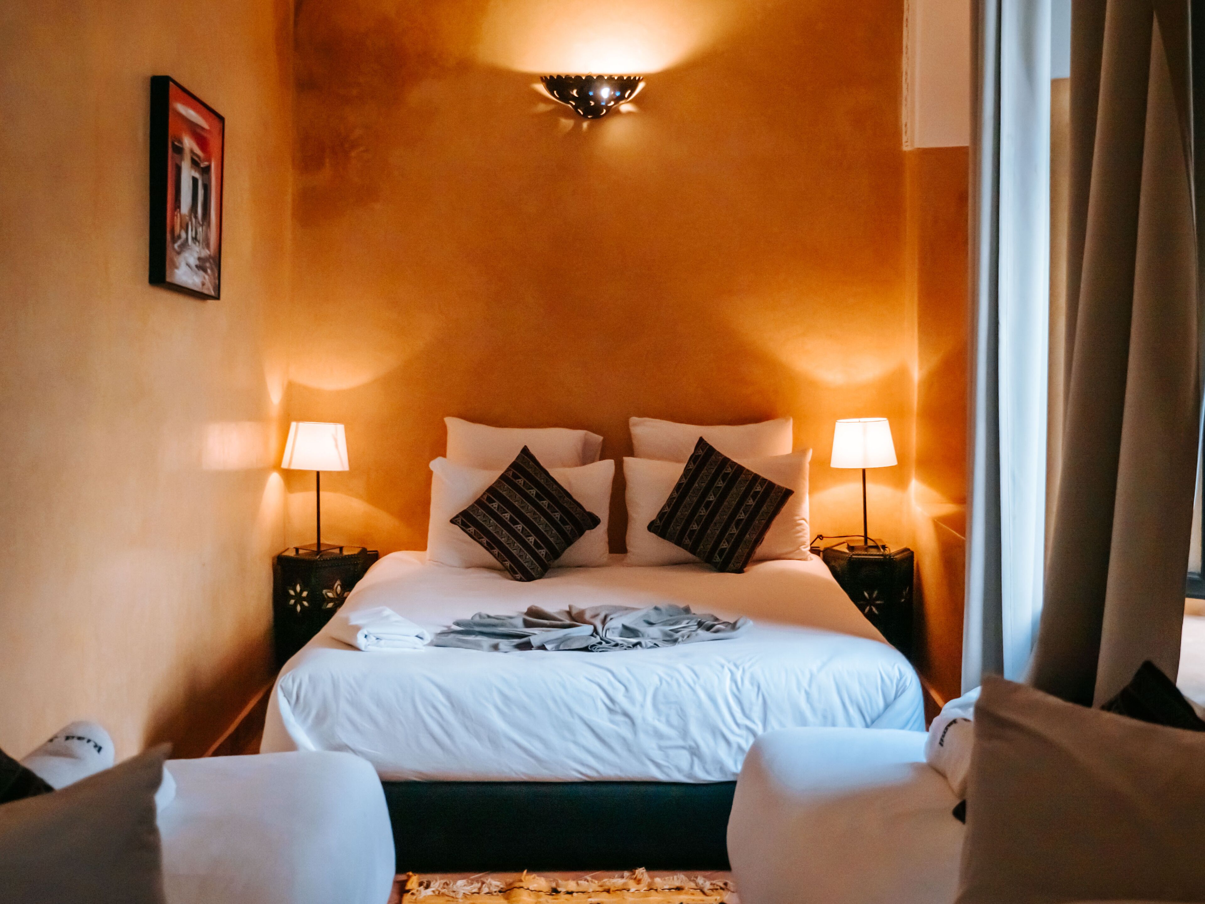 Una habitación de hotel con una cama, dos lámparas de noche, un cabecero y un aplique de pared.