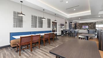 A modern dining area with a long table and chairs, a counter with a television, and a kitchen area in the background.