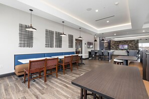 A modern dining area with a long table and chairs, a counter with a television, and a kitchen area in the background. - Holiday Inn Express Kansas City North Parkville (Parkville)