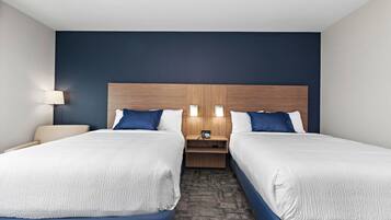 A hotel room with two beds, a wooden headboard, bedside lamps, a nightstand, and a carpeted floor.