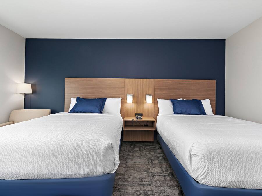 A hotel room with two beds, a wooden headboard, bedside lamps, a nightstand, and a carpeted floor.