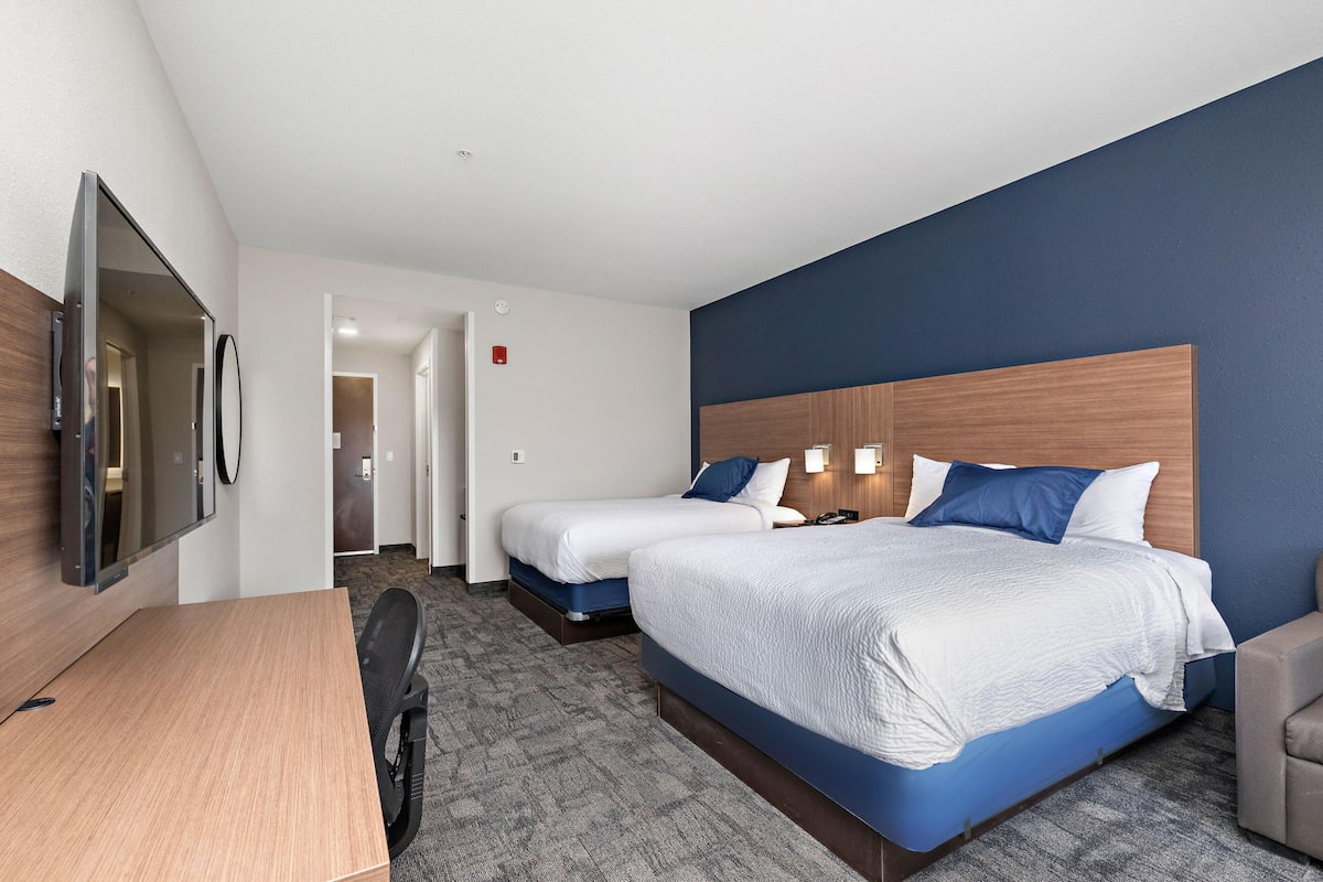 A hotel room with two beds, a desk, and a TV.
