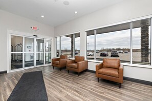 A reception area with a glass door entrance, leather chairs, a black rug, and large windows overlooking a parking lot. - Holiday Inn Express Kansas City North Parkville (Parkville)