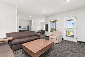 A modern hotel room with a sofa, a small table, a chair, and a balcony door. - Holiday Inn Express Kansas City North Parkville (Parkville)