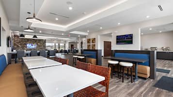 Un restaurant moderne avec des tables blanches, des banquettes marron rembourrées et un mur en pierre en arrière-plan.