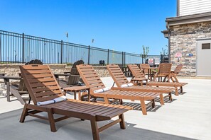 Outdoor lounge chairs and tables arranged on a patio with a stone wall and metal railing in the background. - Holiday Inn Express Kansas City North Parkville (Parkville)