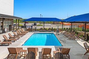 A pool area with lounge chairs and umbrellas, a parking lot, and a building with a stone facade. - Holiday Inn Express Kansas City North Parkville (Parkville)