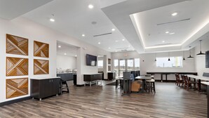 A spacious, modern interior with a wooden floor, a kitchen area, and a dining space with tables and chairs. - Holiday Inn Express Kansas City North Parkville (Parkville)