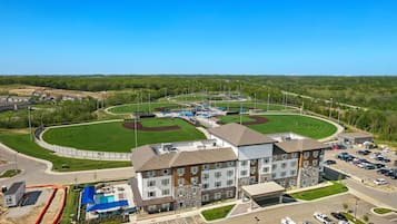 A multi-story hotel with a swimming pool and a baseball field.