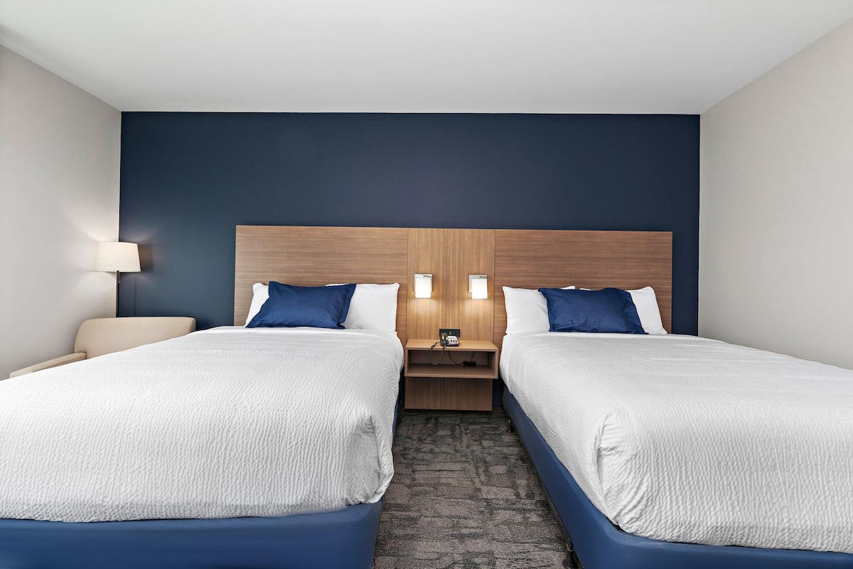 A hotel room with two beds, a wooden headboard, bedside lamps, a nightstand, and a carpeted floor.
