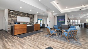 A modern reception area with a wooden reception desk, blue chairs, and a stone wall. - Holiday Inn Express Kansas City North Parkville (Parkville)