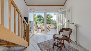 A room with a wooden staircase, a wicker chair, a small table, and a view of an outdoor balcony with chairs and plants. - Beachfront apartment with balcony and parking (Split)