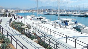 A marina with boats docked, a pedestrian walkway, and a cityscape in the background. - Beachfront apartment with balcony and parking (Split)