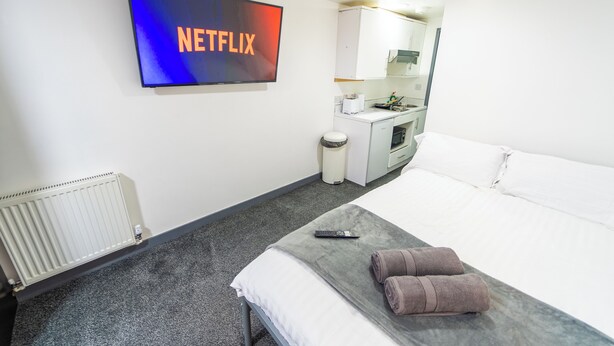 A hotel room with a bed, a TV mounted on the wall, a small kitchenette, and a radiator. - Beautiful 1-Bed Studio in Birmingham (Birmingham)