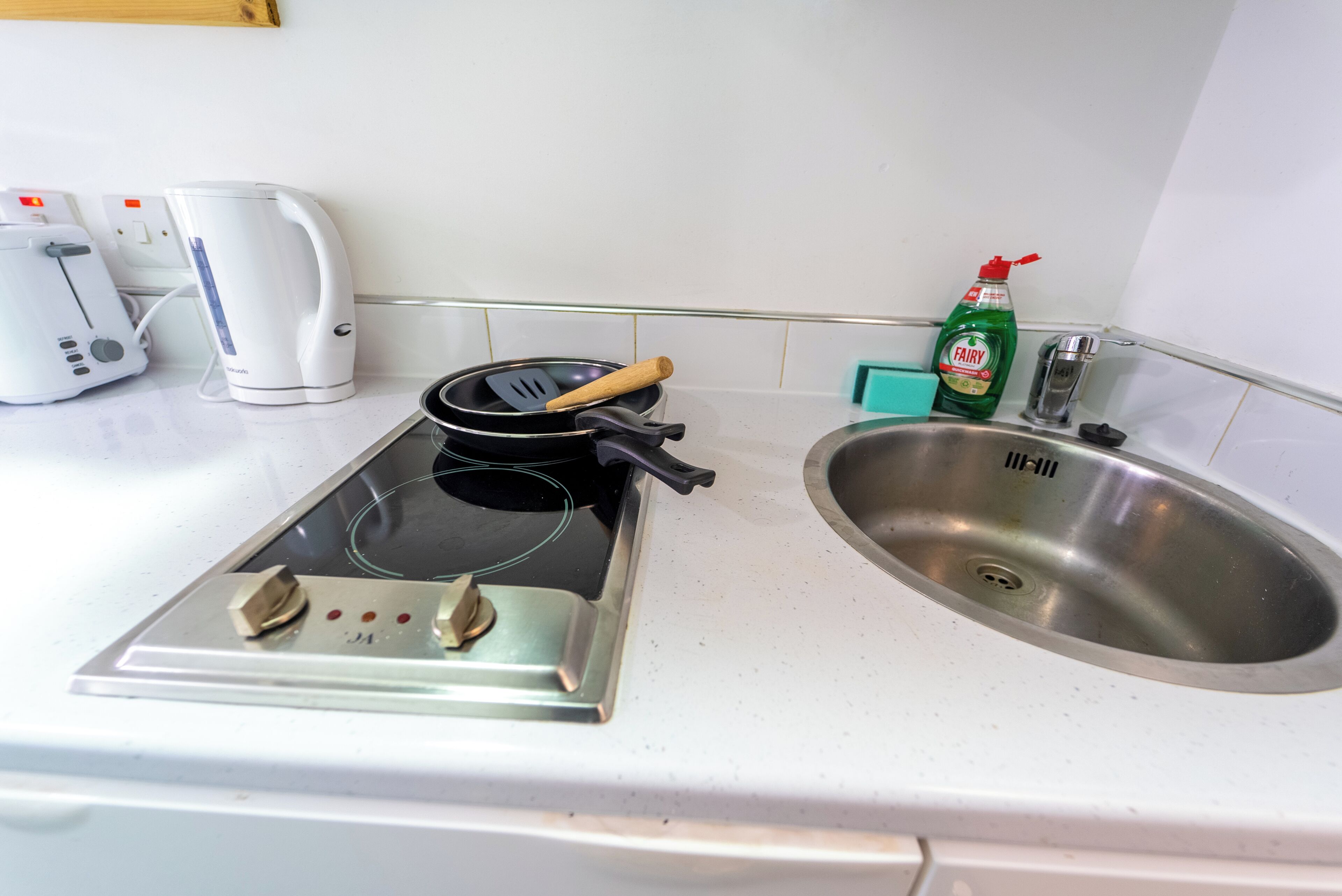 A kitchen with a stove, a sink, a toaster, a kettle, and a dish soap bottle.