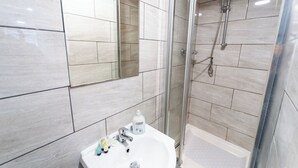 A modern bathroom with a glass-enclosed shower, a white sink with toiletries, and a mirror above the sink. - Beautiful 1-Bed Studio in Birmingham (Birmingham)
