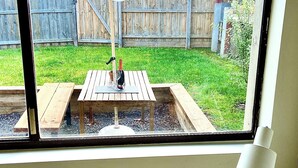 A window view of a backyard with a wooden deck, picnic table, and umbrella. - 🔆PINEPLACE🔆BFast,Wi-Fi,Walk2Pizza,Coffee,Liquor (Norlane)