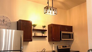 A kitchen with a refrigerator, microwave, stove, and a hanging light fixture.