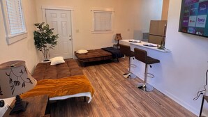 A compact living space with a kitchenette, a sofa, a dining table, and a TV mounted on the wall.
