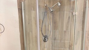 A glass-enclosed shower with a showerhead and hose, a toilet with a paper towel holder, and a pebble-patterned floor.