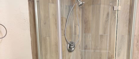 A glass-enclosed shower with a showerhead and hose, a toilet with a paper towel holder, and a pebble-patterned floor.