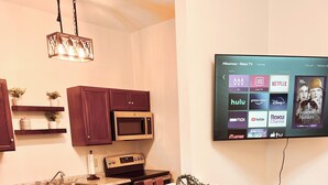 A modern kitchen with a central island, bar stools, a microwave, and a flat-screen TV displaying streaming services.