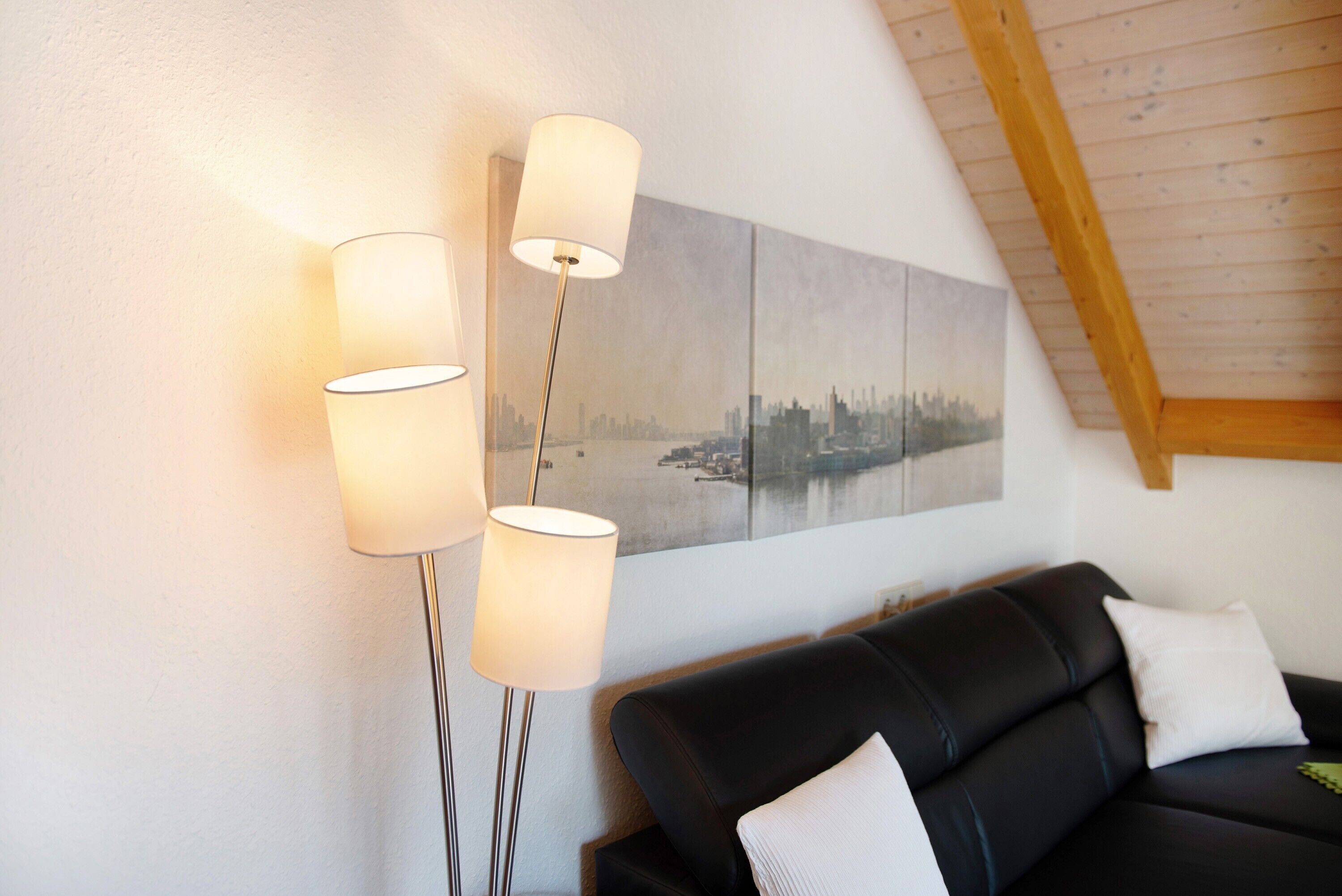 A modern living room with a black leather sofa, a cityscape painting, and three floor lamps.