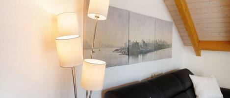 A modern living room with a black leather sofa, a cityscape painting, and three floor lamps.