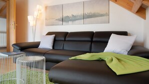 Een moderne woonkamer met een zwarte leren bank, een groene plaid en een stadsgezichtschilderij aan de muur.
