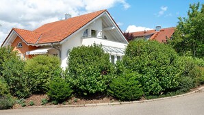 Een huis met een rood pannendak, omgeven door weelderige groene struiken.