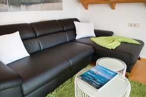A modern living room with a dark leather sofa, a white round coffee table with a book, and a green throw blanket.