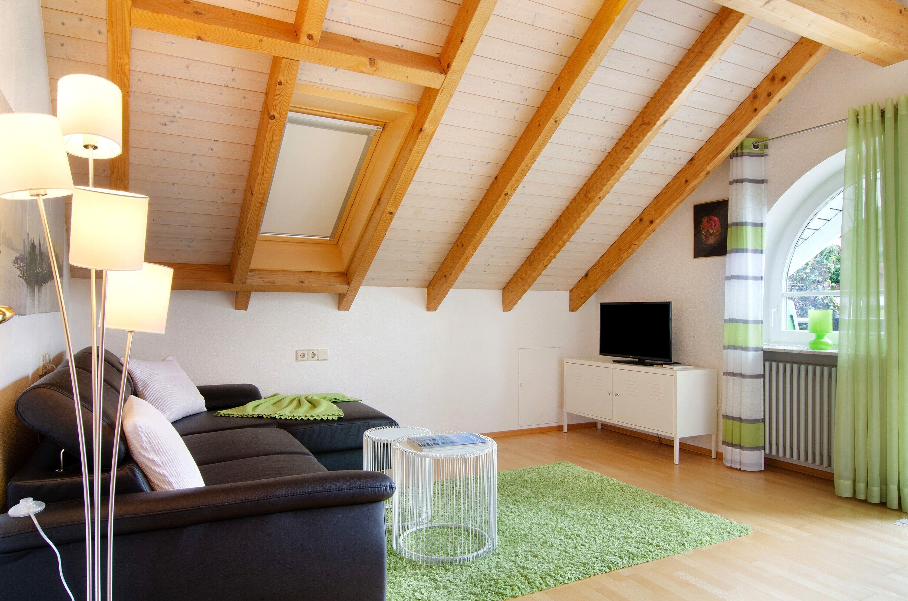 A modern living room with a sloped ceiling, a sofa, a television, a white cabinet, and a radiator.
