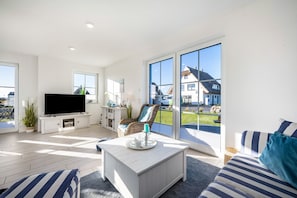 A modern living room with a flat-screen TV, a coffee table, a sofa, and a large sliding glass door leading to an outdoor area.