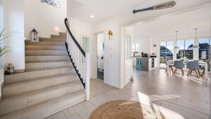 A modern interior with a staircase, a dining area with chairs, and a kitchen visible through an open door. - Holiday Home 'Ankerplatz' with Sea View, Sauna, and Gas Fireplace (Dranske)