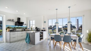 A modern kitchen with a large island, dining area with chairs, and large windows offering a view. - Holiday Home 'Ankerplatz' with Sea View, Sauna, and Gas Fireplace (Dranske)