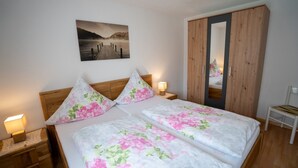 A bedroom with a wooden headboard, two floral-patterned bedsheets, a nightstand with a lamp, a wooden wardrobe, and a painting on the wall. - Holiday Apartment "Haus Franziska" with Mountain View, Private Terrace & Wi-Fi (Todtnau /Brandenberg)