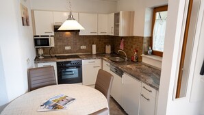 A compact kitchen with a microwave, oven, sink, and a dining area with a table. - Holiday Apartment "Haus Franziska" with Mountain View, Private Terrace & Wi-Fi (Todtnau /Brandenberg)