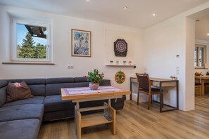 Ein modernes Wohnzimmer mit einer Couch, einem Holztisch mit Pflanze, einem Dartspiel und einem Bild an der Wand.