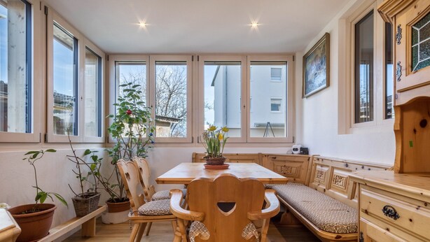 Un comedor con mesa y sillas de madera, plantas en macetas y un banco.
