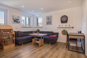Ein modernes Wohnzimmer mit einer Couch, einem Holztisch, einer Dartscheibe und einem Bücherregal.