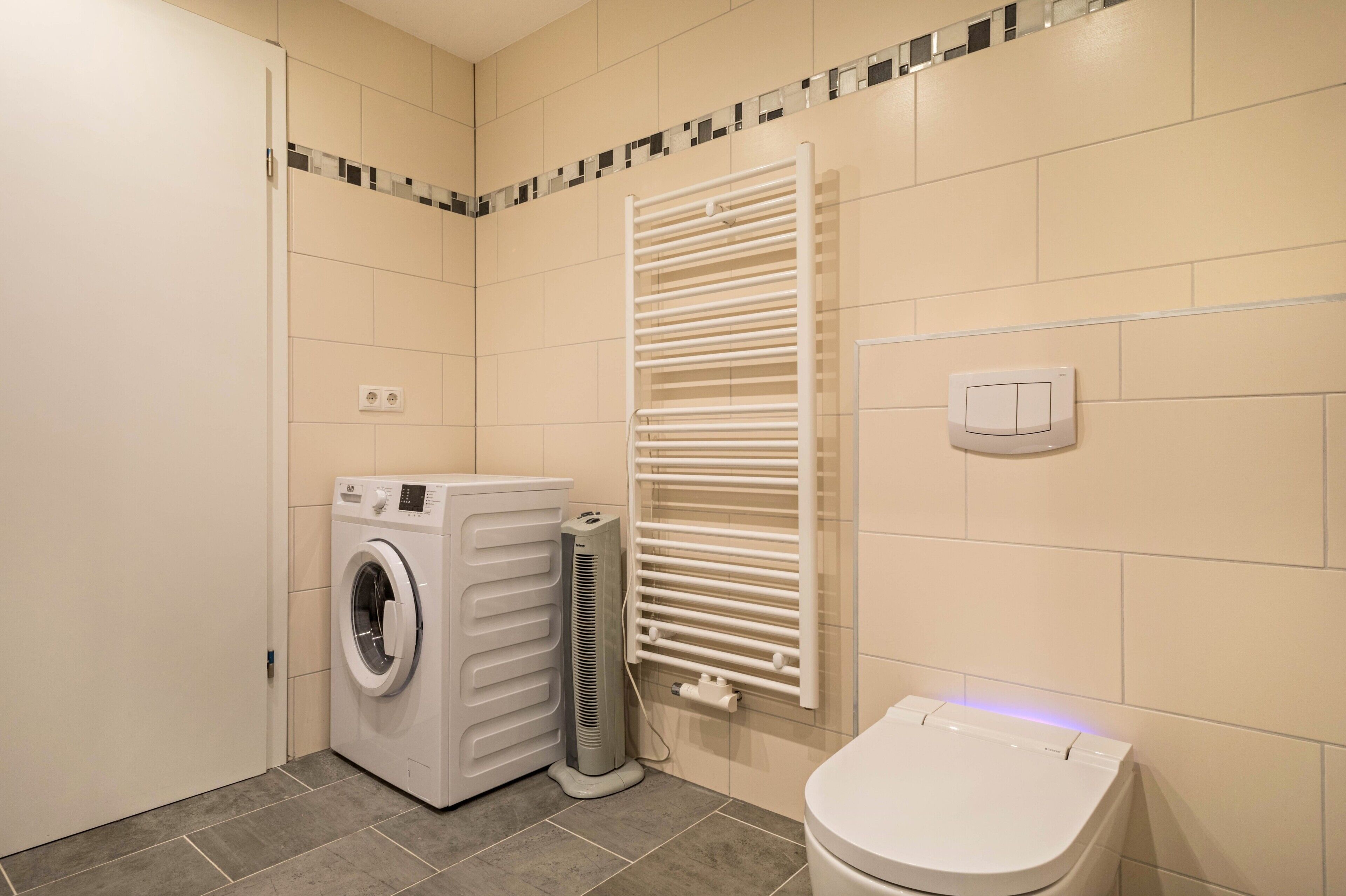 A compact bathroom with a washing machine, a radiator, and a toilet.
