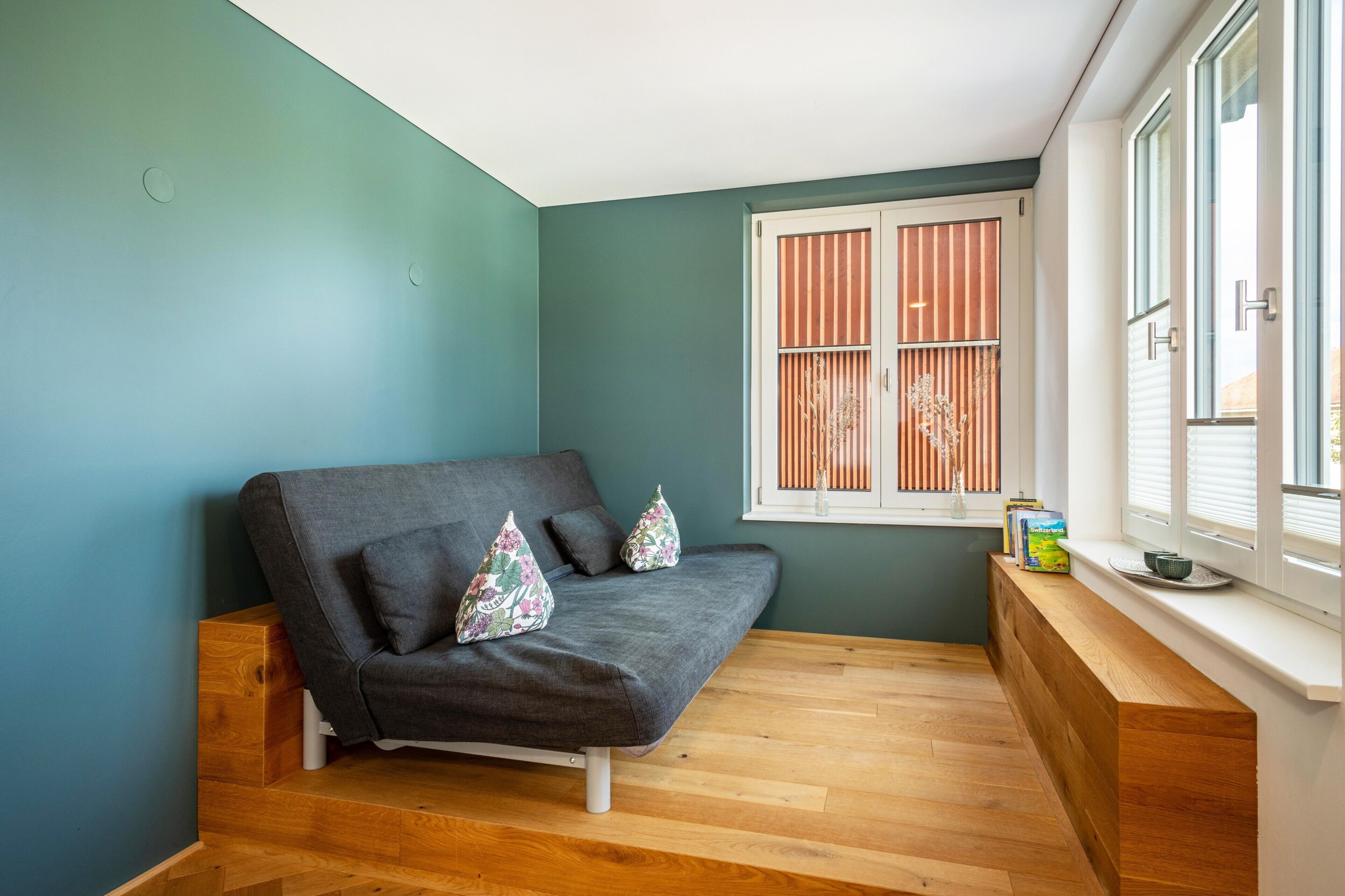 A room with a grey sofa, wooden bench, and a window with blinds.